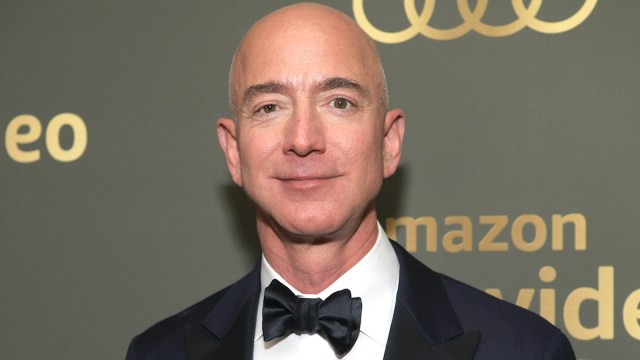 Jeff Bezos in a black and white suite, black bow tie, and standing in front of a blurred green background