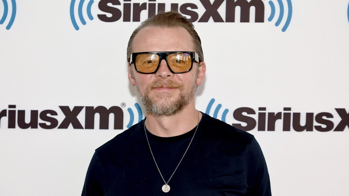 Comedian Simon Pegg visits Sirius XM wearing sunglasses and a necklace over a dark sweater.