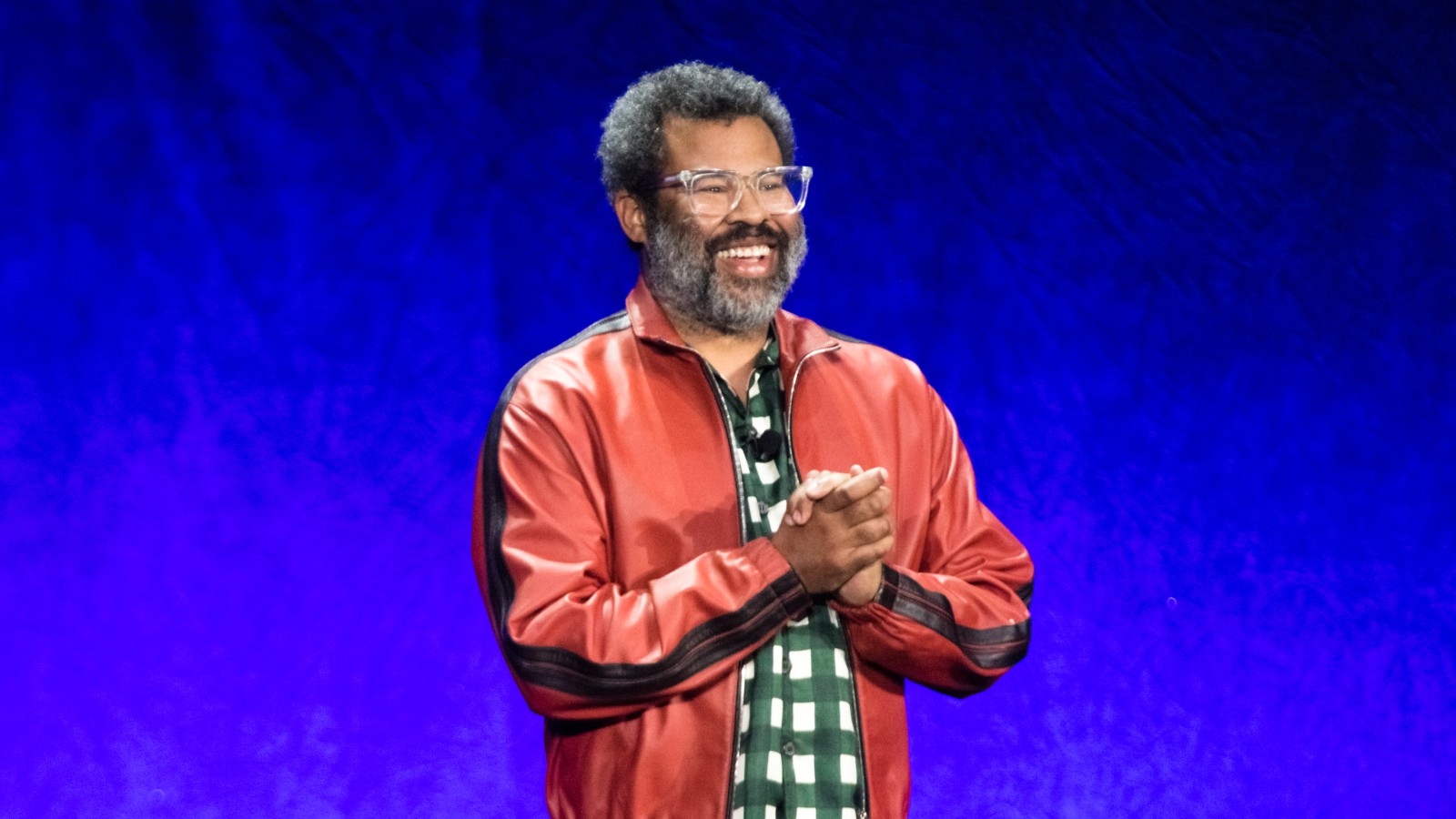 Jordan Peele gives a talk on a stage against a blue background.