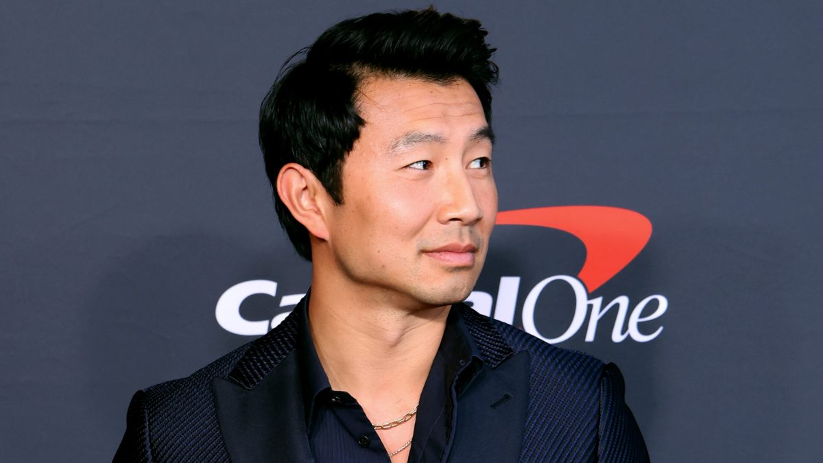 Simu Liu in a shoulders-up portrait in dark shirt and jacket, smiling slightly and looking off-camera