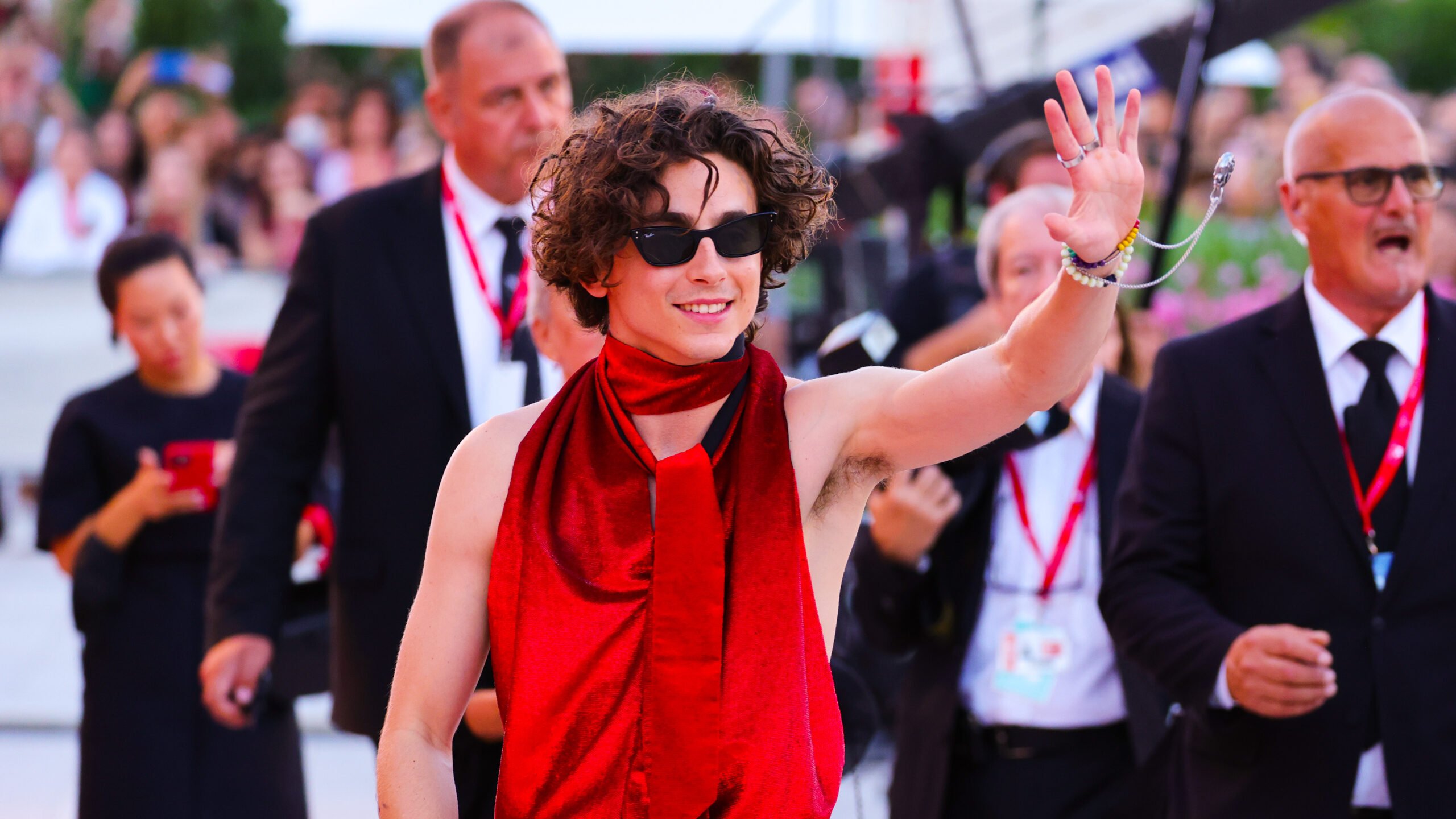 Timothée Chalamet attends the "Bones And All" red carpet at the 79th Venice International Film Festival on September 02, 2022 in Venice, Italy wearing a blood red sleeveless jumpsuit and waving at his fans