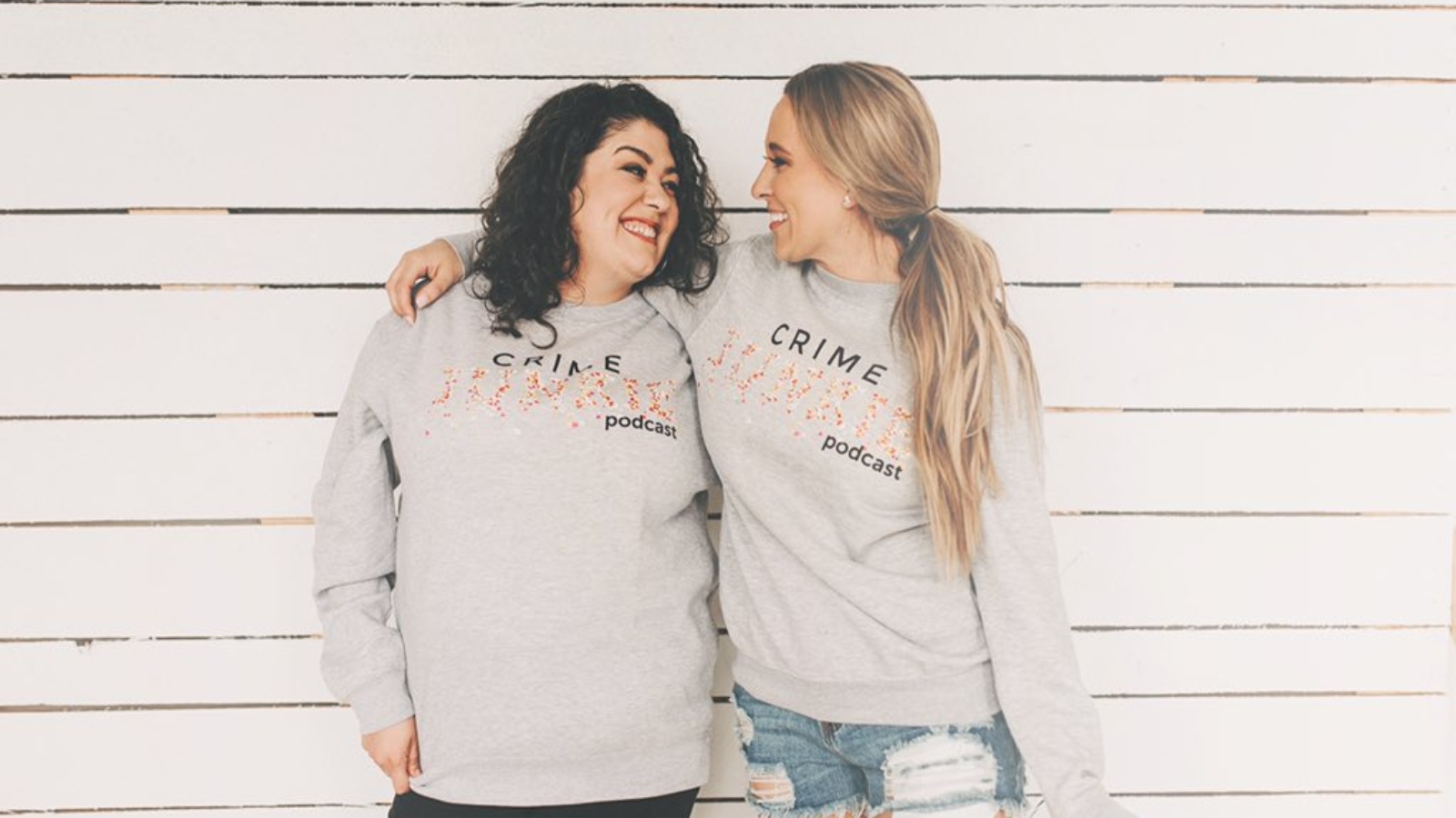 Ashley Flowers with her arm around Brit Prawat, both in matching Crime Junkie Podcast sweatshirts