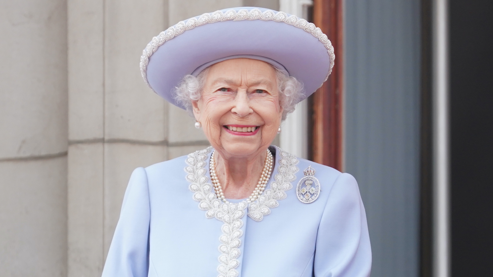 Queen Elizabeth II dressed in a lavender jacket and hat watches from the balcony of Buckingham Palace