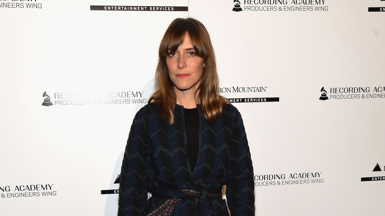 Feist attends Grammys celebration in a dark coat and red dress.