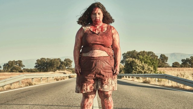 A woman is standing in the middle of the street covered in blood.