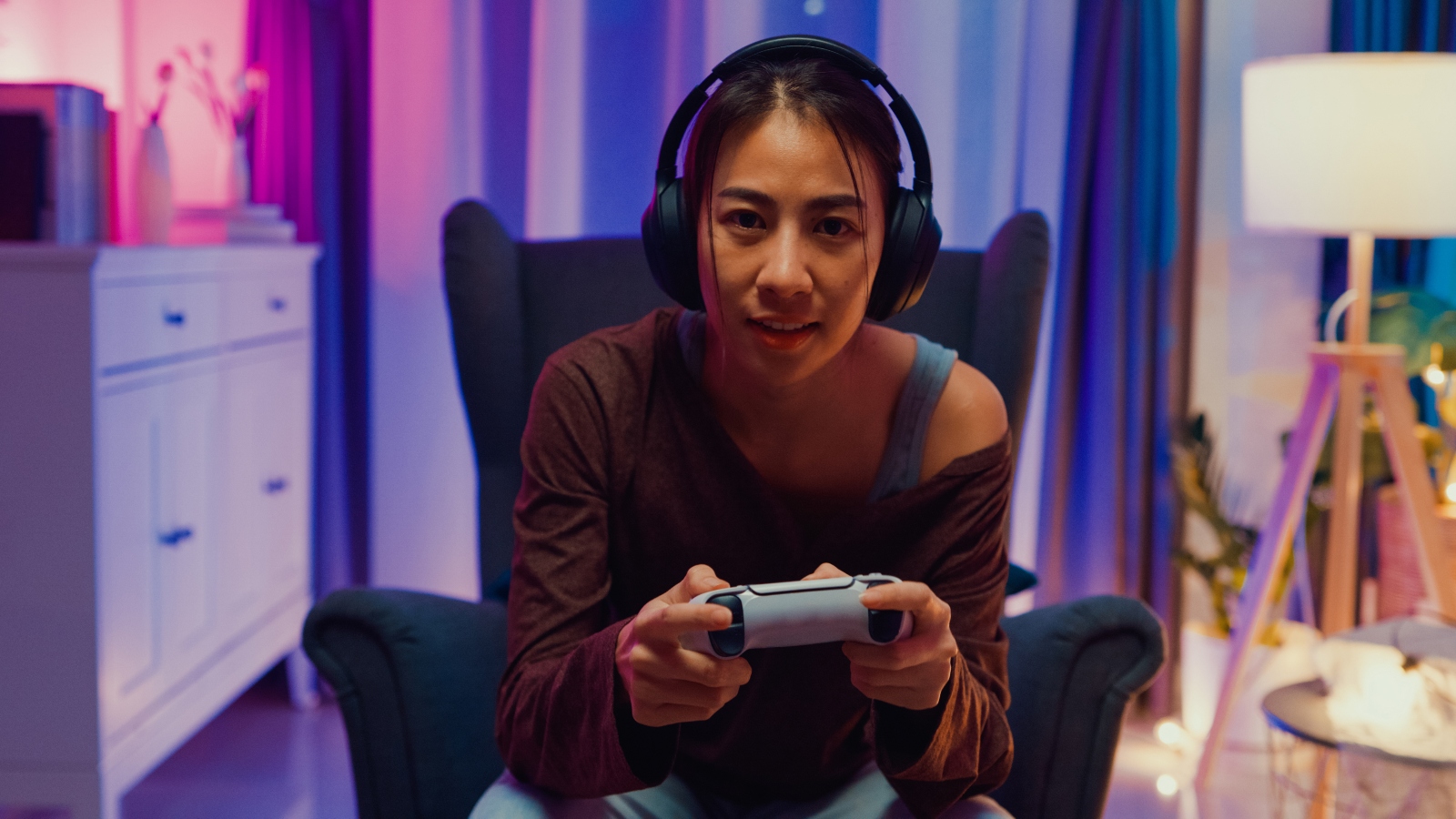 Happy young Asian woman wear casual sit on sofa chair hold joystick controller exciting and shouting while having fun winning playing video game sit on sofa in the living room home at night. - stock photo