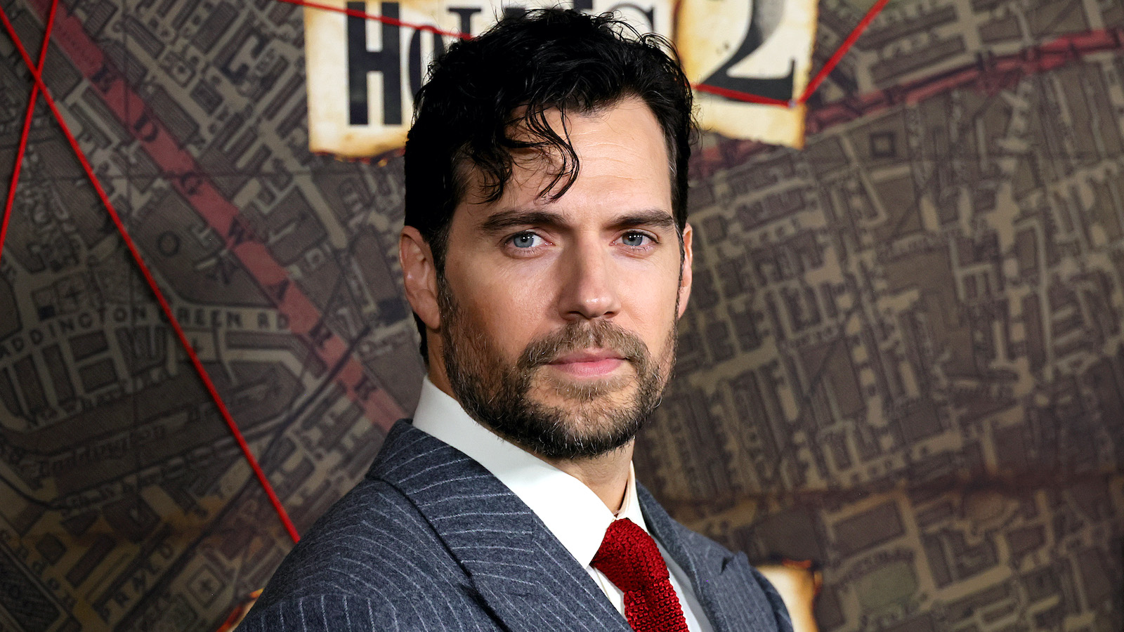 Henry Cavill on the red carpet wearing a blue suit, white shirt, and red tie