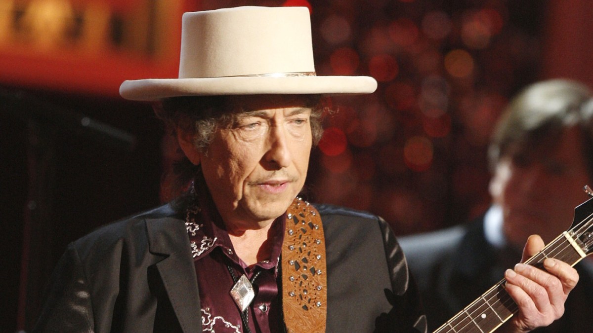 Bob Dylan plays a guitar on stage at a concert.