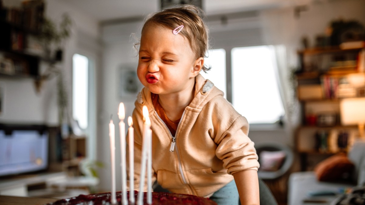 Little birthday girl blowing out candles on cake at home - stock photo