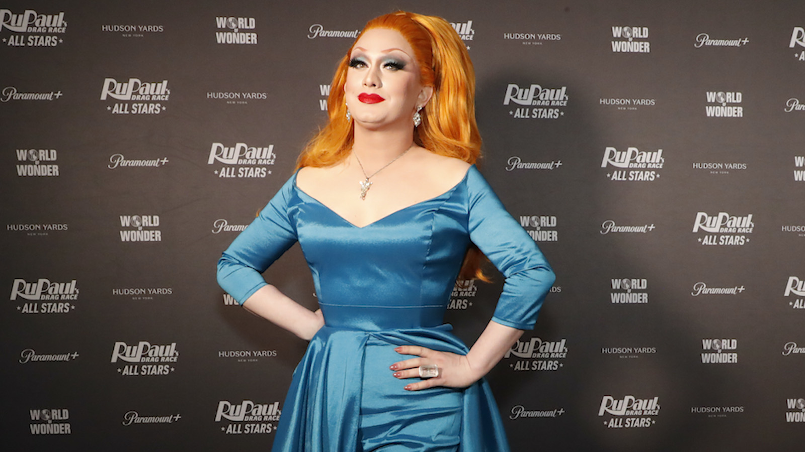 Jinkx Monsoon wearing a teal dress and signature red wig on the red carpet