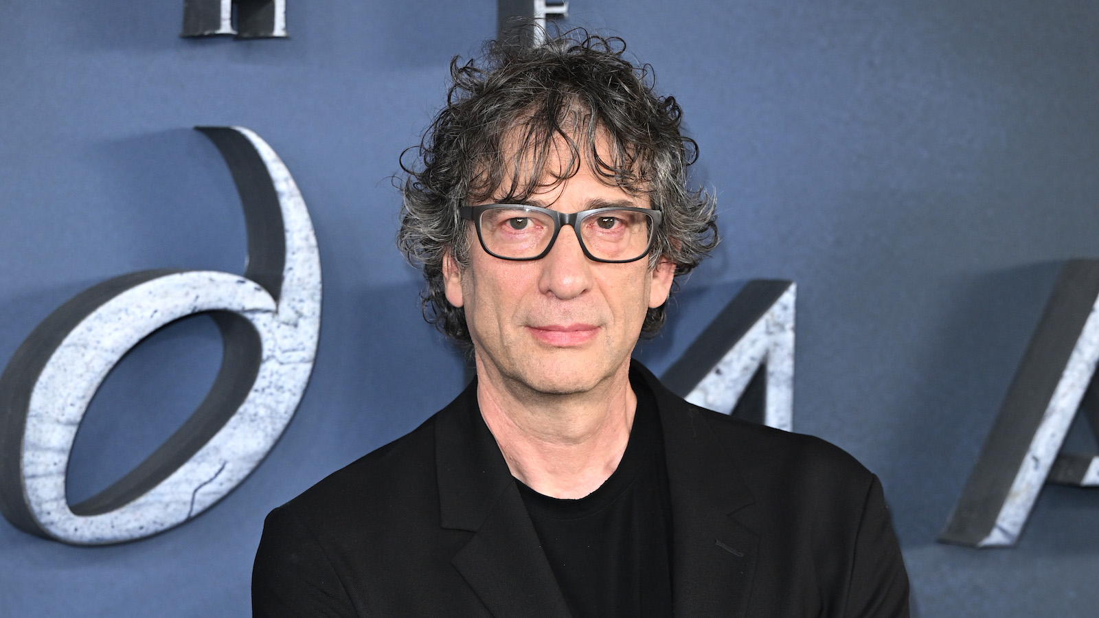 Neil Gaiman on the red carpet wearing an all black shirt and blazer