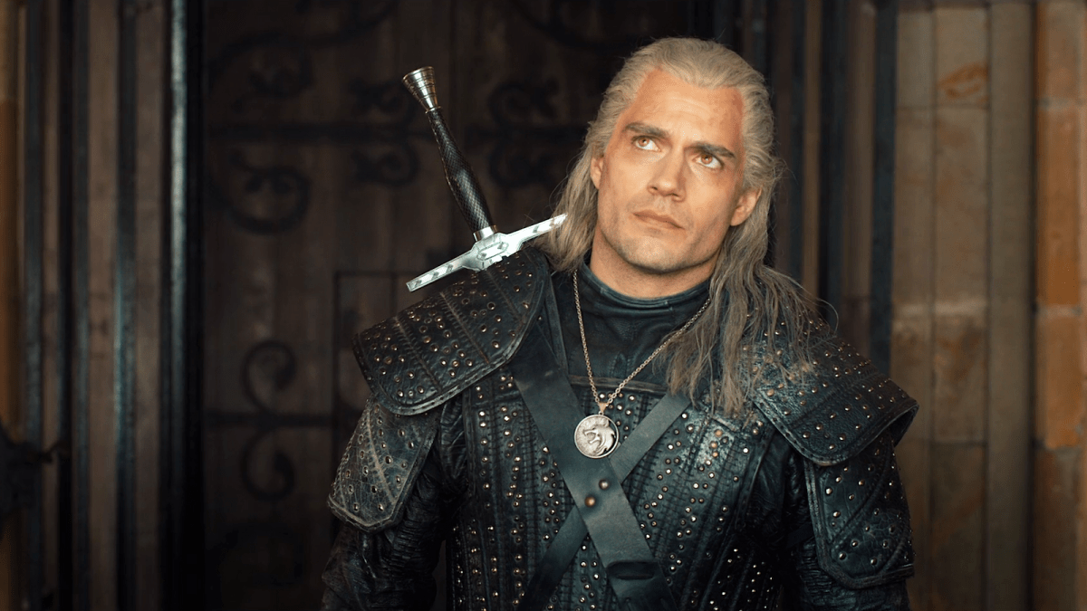 Geralt of Rivia (Henry Cavill) in black armour, white hair, and sword sheathed behind his back