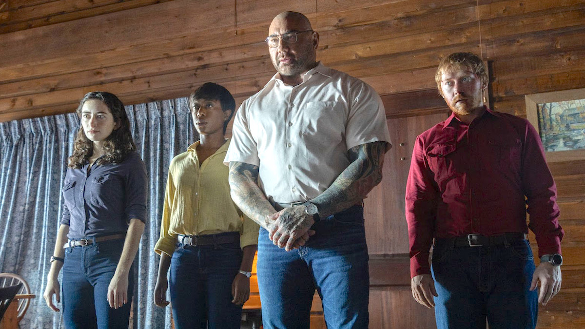 The four strangers from 'Knock at the Cabin' stand forebodingly shoulder to shoulder (Abby Quinn as Adriane, Nikki Amuka-Bird as Sabrina, Dave Bautista as Leonard Brocht,and Rupert Grint as Redmond)