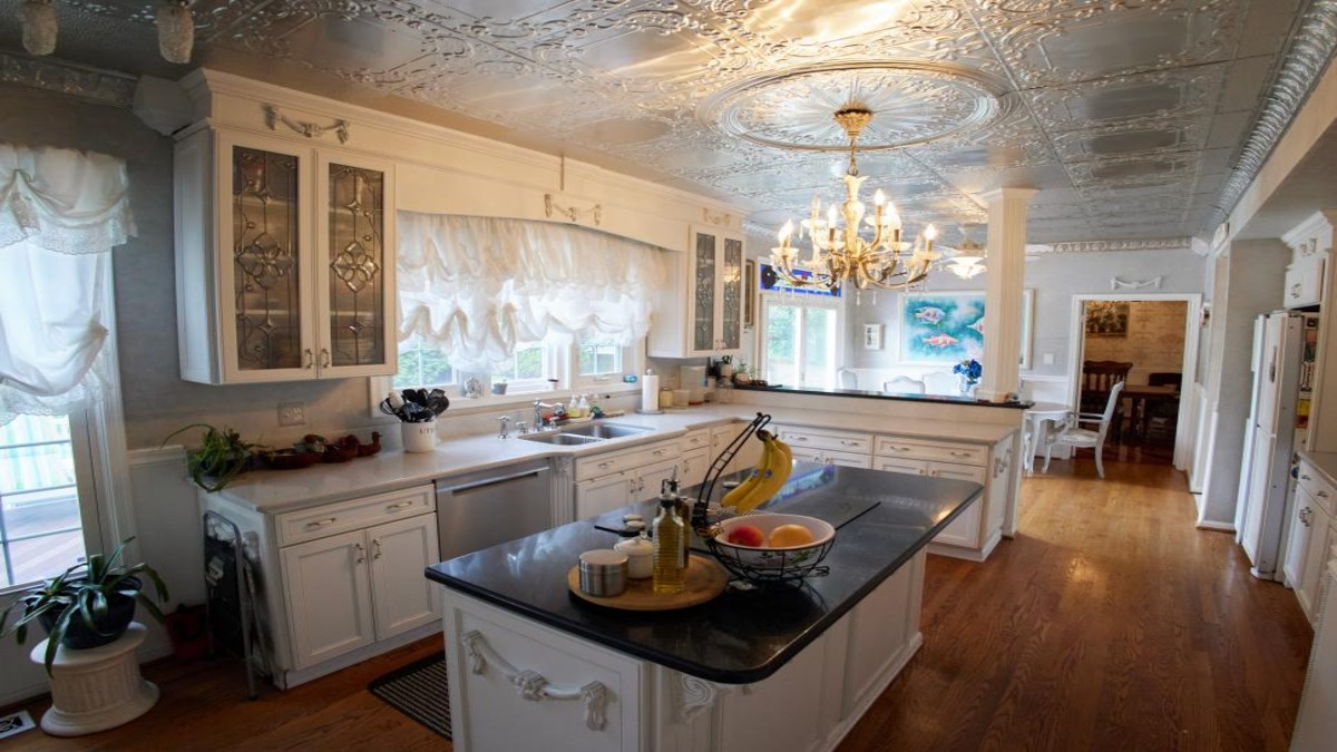 An ornate kitchen with tin ceiling and sparkly chandelier and flouncy window treatments.