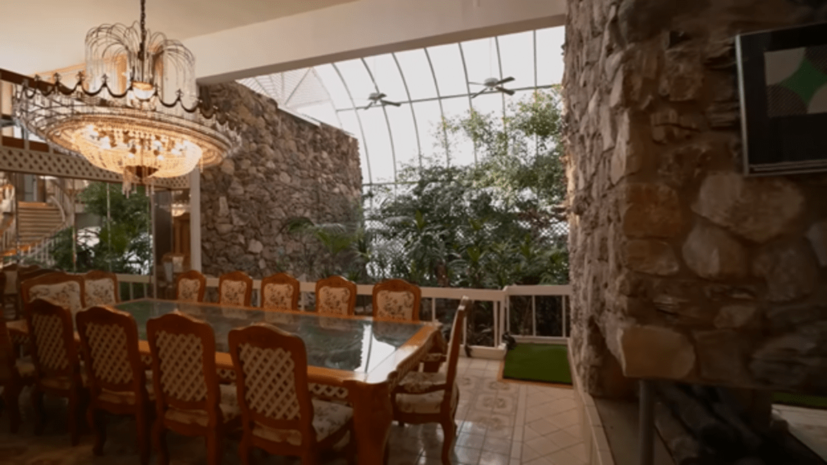 A dining room with stone walls and a jungle-like greenhouse and gaudy chandelier. 