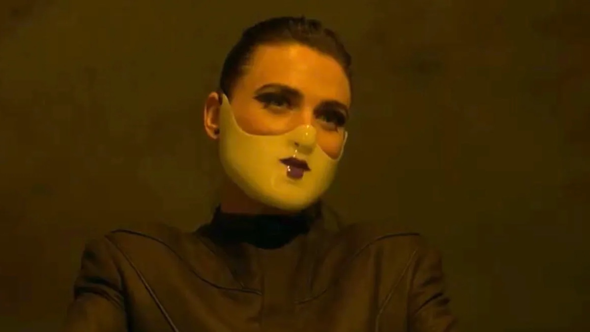 Katie McGrath as The Adjudicator, wearing a mask on the lower half of her face