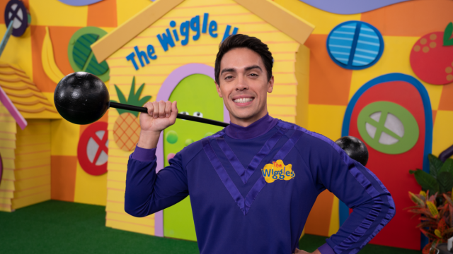 A photograph of John Pearce, the Purple Wiggle in The Wiggles, holding his weights whilst standing in front of The Wiggle House.