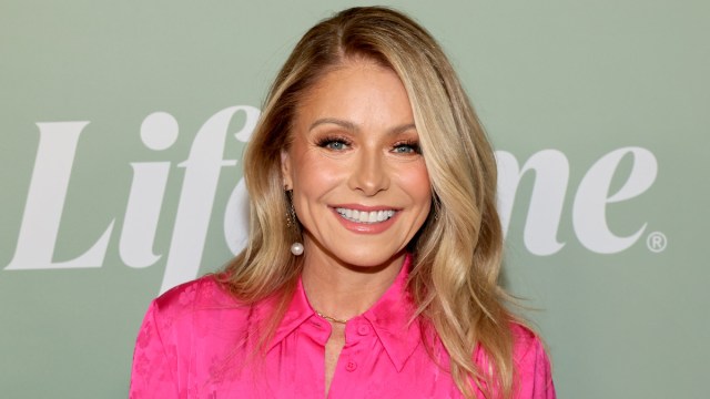 Kelly Ripa wearing a hot pink blouse and standing in front of a light green background